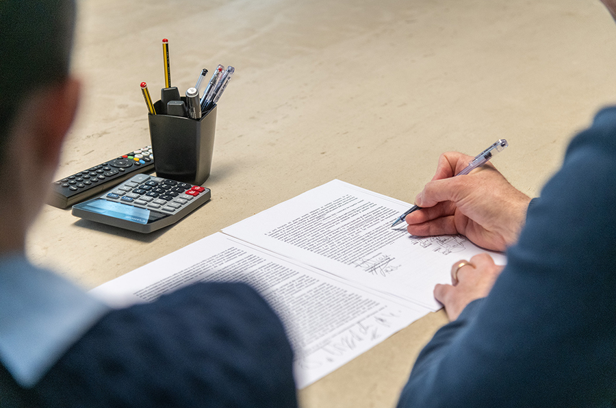 Un professionista dello Studio Sette firma documenti, con calcolatrice e telecomandi sul tavolo, simbolo di consulenza del lavoro e gestione del personale.