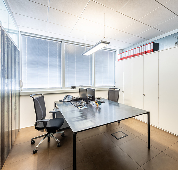 Ufficio moderno e luminoso dello Studio Sette con scrivania, sedie ergonomiche, computer e armadietti, riflettendo professionalità e organizzazione.