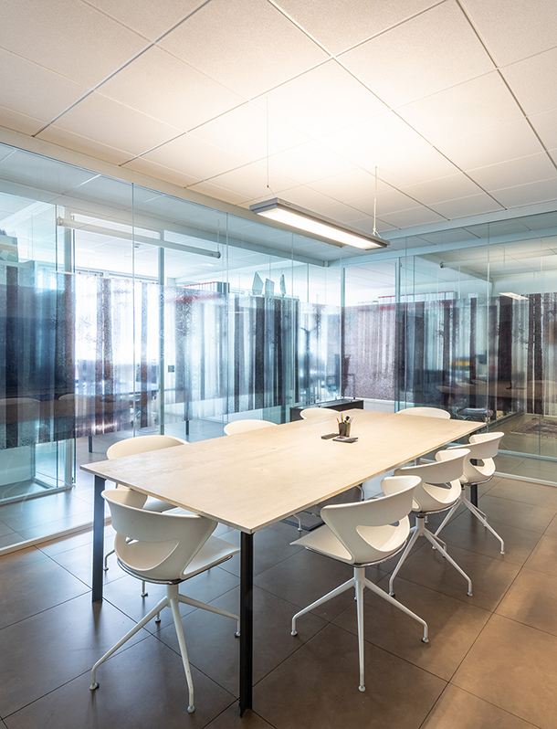 Moderna sala riunioni dello Studio Sette con tavolo rettangolare e sedie bianche, circondata da pareti in vetro.